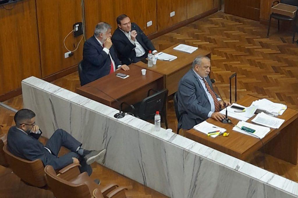 tres personas sentadas en una sala de tribunales.