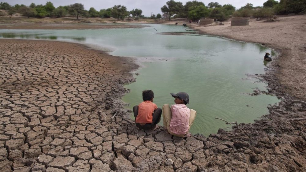 dos niños contemplan lo que queda de un río seco.