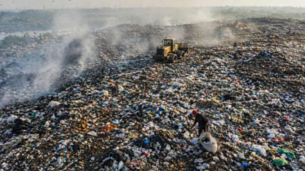 Basural a cielo abierto con montañas de residuos, humo en el ambiente, una topadora y una persona recolectando materiales reciclables