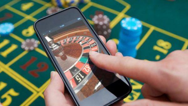 una mano tirando la ruleta en un celular y de fondo un tablero de poker con fichas