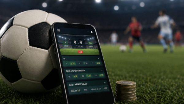 celular apoyado sobre una pelota de fútbol, detrás dos hombres jugando. (Crédito: Archivo)