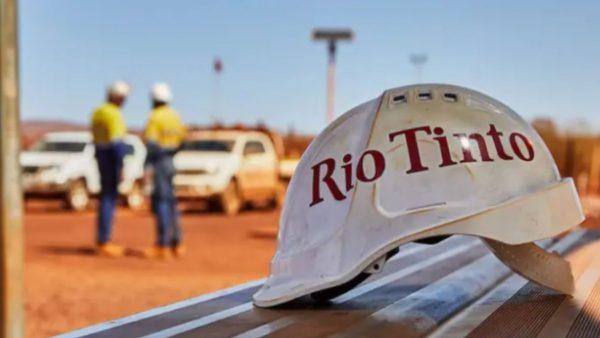 caso en primer plano con la leyenda Rio Tinto. Detrás dos operarios con dos camionetas blancas.
