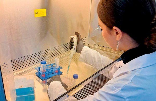 Una mujer con guardapolvo blanco toma una jeringa para color una sustancia en tubos de ensayos en un laboratorio. Crédito: UBA