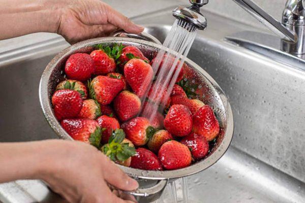 dos manos sostienen un bowl de frutillas mientras son lavadas en la pileta de una cocina. (Crédito: .istockphoto)