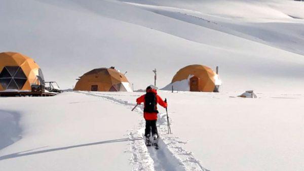 Un hombre camin sobre la nieve, detrás un campamento con tres carpas. Imagen: El Azufre