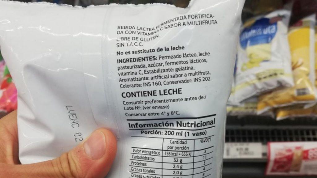 Una mano agarra un sachet de leche y muestra los ingredientes.