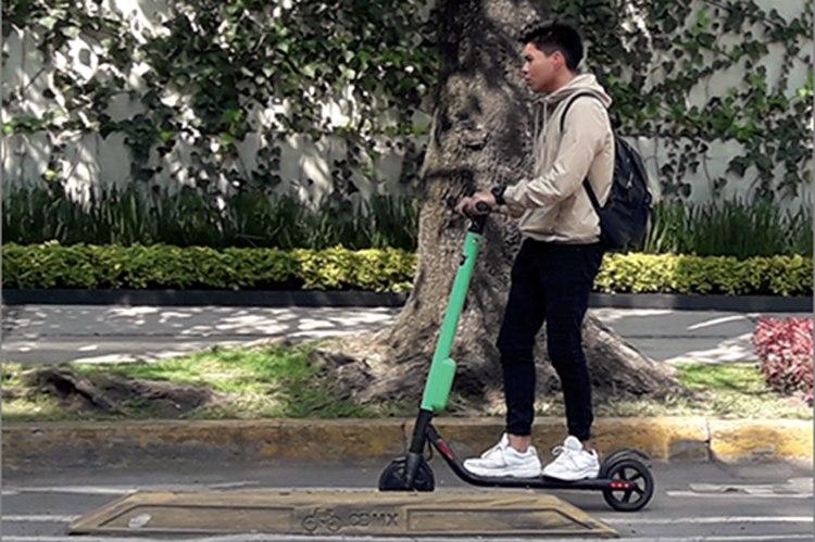 Un joven arriba de un monopatín eléctrico andando en la calle.