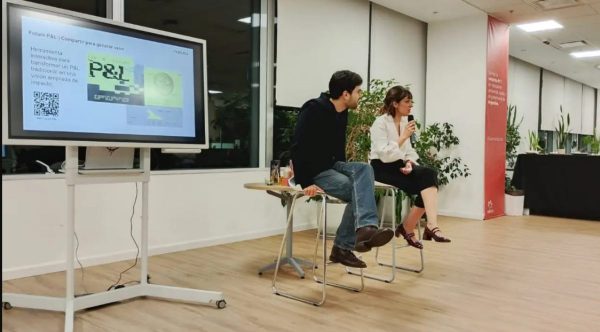 Dos personas sentadas al lado, una pantalla. (Crédito: Natura)