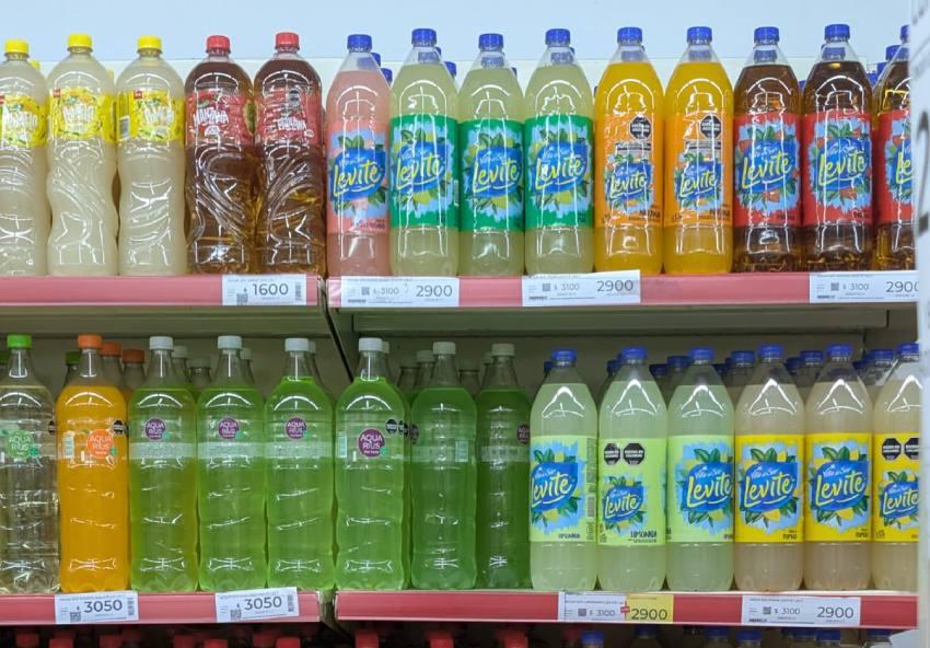 Un primer plano de estantes de supermercado bien iluminados, repletos de botellas de plástico de bebidas de colores