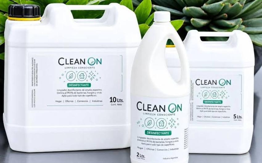 Tres envases plásticos blancos de desinfectante marca Clean On en presentaciones de 10, 5 y 2 litros, sobre un fondo con plantas verdes.