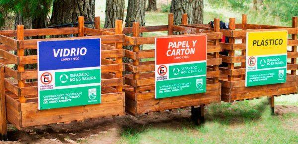Tres contenedores de madera para reciclaje en un parque o zona arbolada.
