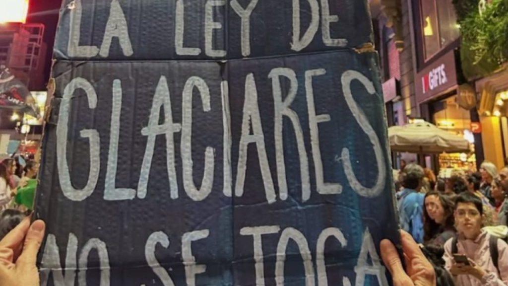 Un cartel con la leyenda "la ley de glaciares no se toca" sostenido por dos manos en el medio de una manifestación