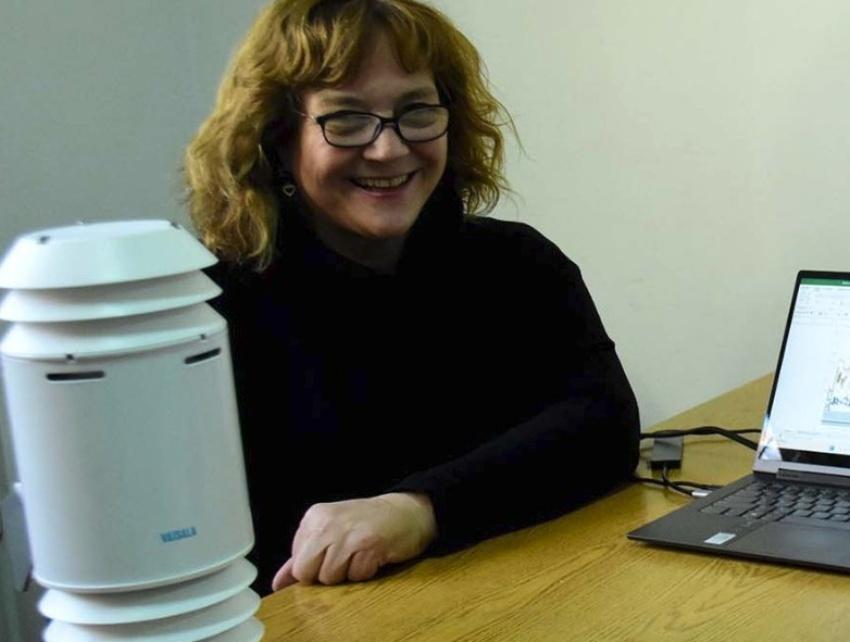 Marisa Cogliati sonríe sentada junto a un escritorio en el que se aprecia un sensor de medición meteorológica y de aire blanco junto a una computadora portátil.