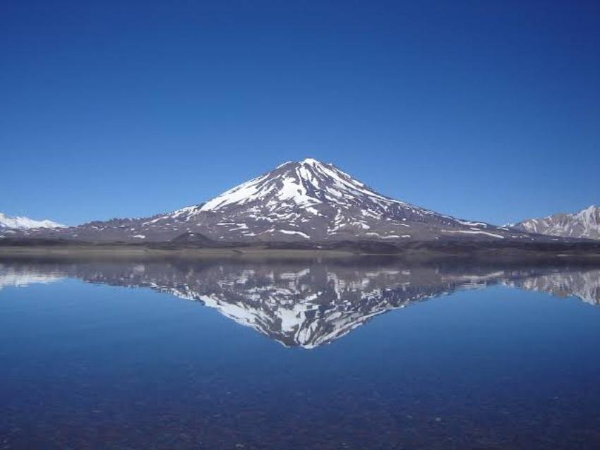 Una montaña nevada reflejada perfectamente en las aguas cristalinas de un lago bajo un cielo azul despejado.