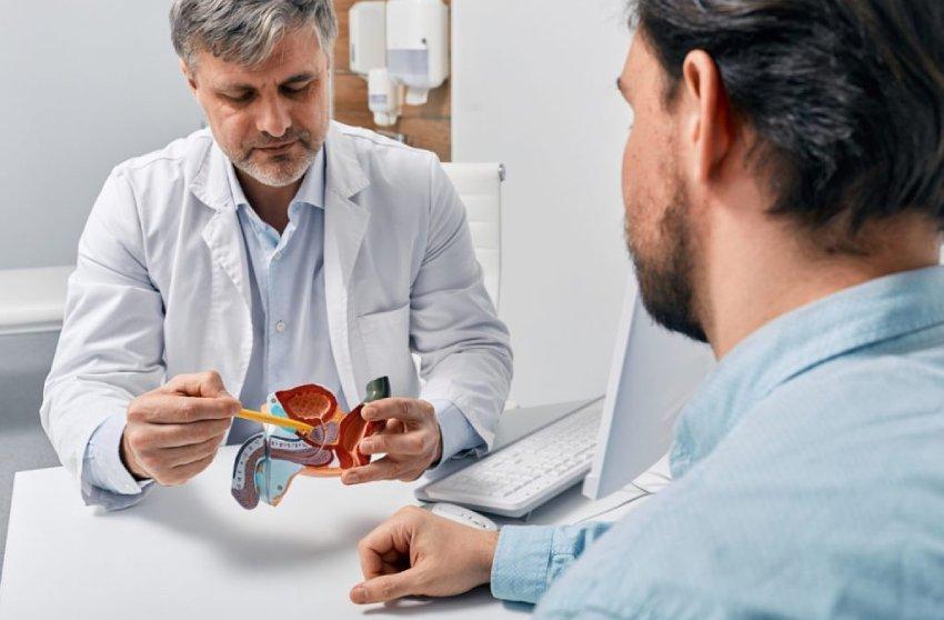 Dos hombres en una mesa. Uno es un médico y sostiene en la mano un objeto.