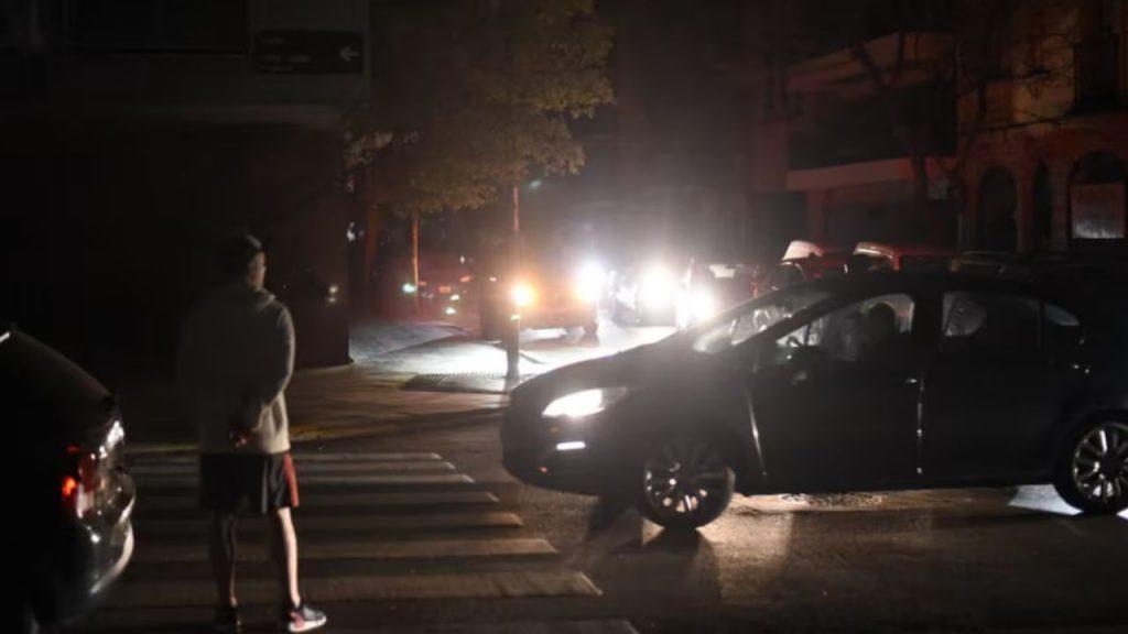 Una esquina de CABA a oscuras, y solo iluminada por las luces de los autos mientras una persona espera para cruzar