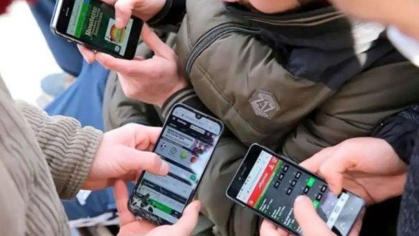 tres pares de manos sostienen un celular cada una de ellas.y se observa una app de apuestas en las pantalas