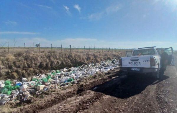 Camioneta policial estacionada junto a una zanja llena de bidones de plástico y basura acumulada en un camino rural bajo un cielo despejado.