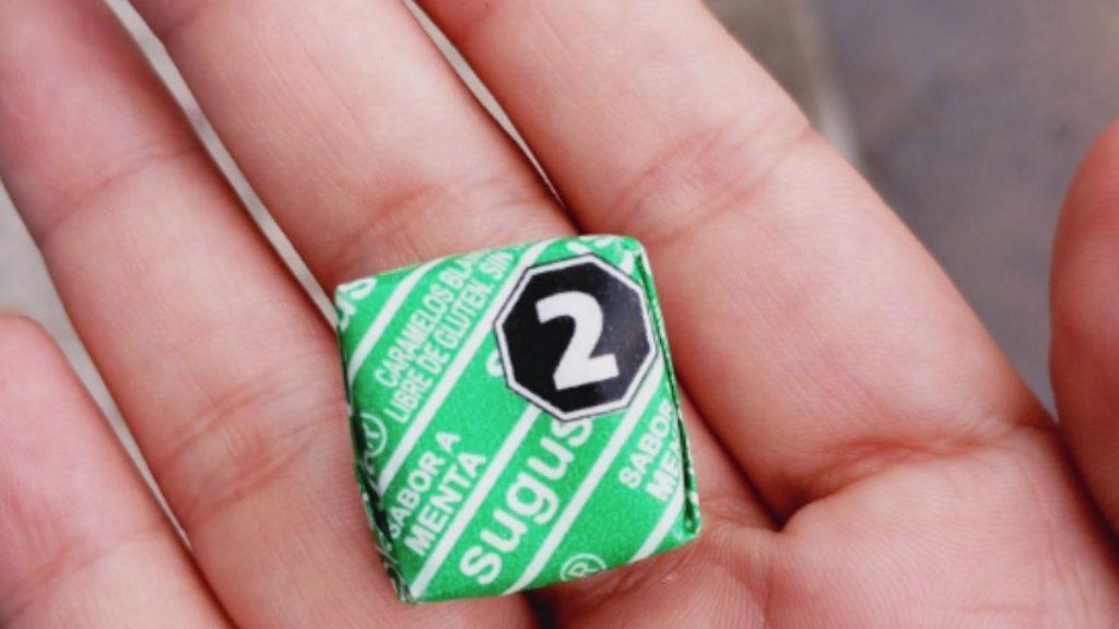 una mano muestra un caramelo de menta de sugus con un octógono