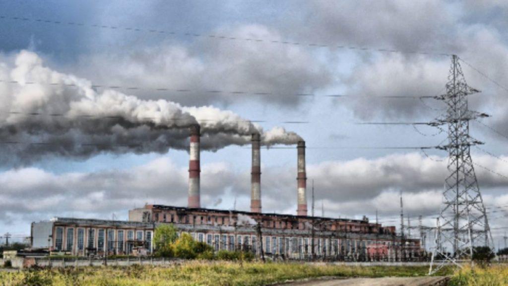 una planta industrial con tres chimeneas en acción expulsando humo contaminante