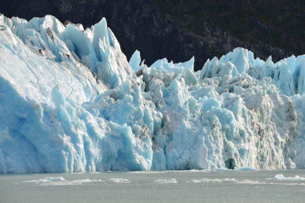 Un cuerpo de agua tranquila y grisácea ocupa el margen inferior, con pequeños trozos de hielo flotando dispersos en la superficie
