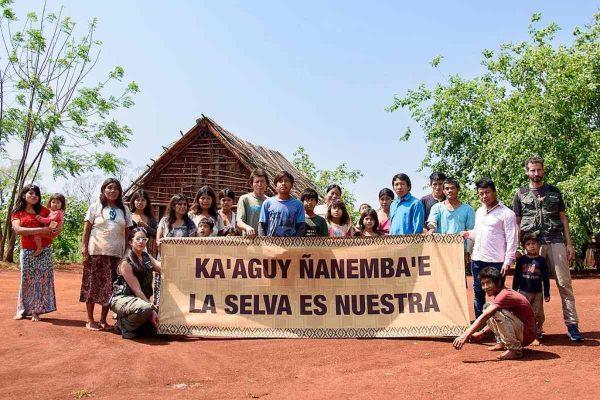 Un grupo de personas de una comunidad indígena mbya guaraní posa al aire libre sosteniendo una pancarta reivindicativa.