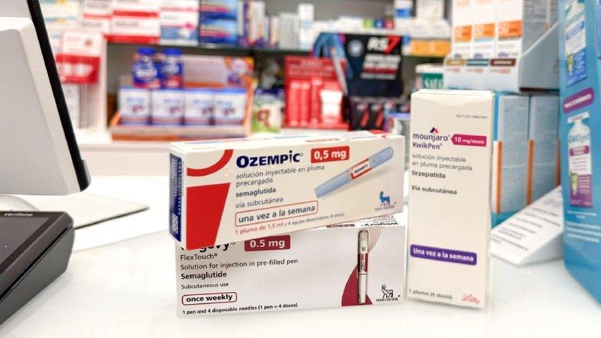 Tres cajas de medicamentos inyectables (Ozempic 0,5 mg, Wegovy 0,5 mg y Mounjaro 10 mg/dosis) dispuestas sobre el mostrador de una farmacia, con estantes llenos de productos farmacéuticos desenfocados al fondo.