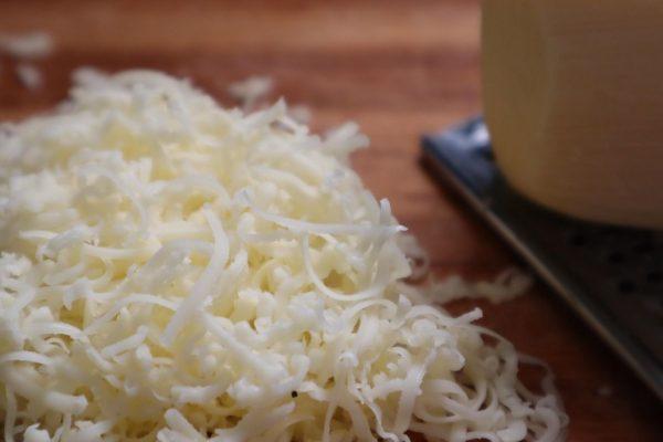 Primer plano de queso rallado sobre una superficie de madera, junto a un rallador.