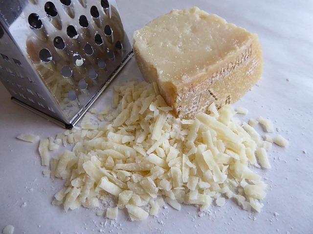 Primer plano de queso rallado sobre una superficie de madera, junto a un rallador.