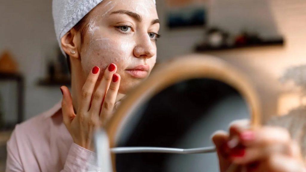 una chica mirándose al espejo y haciendose el skin care con una crema