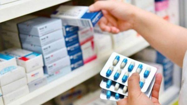 la mano de una persona tomando una caja de medicamentos, mientras que en la otra tiene varios blister de una medicina