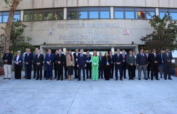 Foto de grupo en el exterior del edificio de la "Escuela Nacional de Protección Civil - Ministerio del Interior". Una amplia delegación de autoridades y representantes, vestidos con trajes formales y chaquetas, posan alineados en fila frente a la entrada principal del establecimiento institucional.