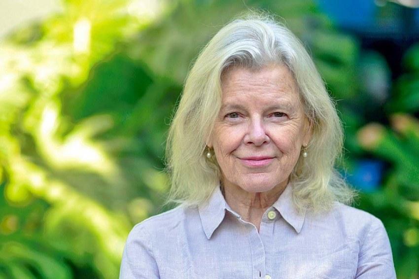Retrato de primer plano de la conservacionista Kristine Tompkins, sonriendo con un fondo natural verde desenfocado.