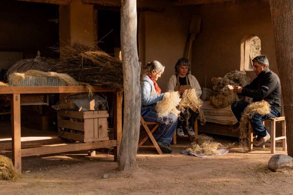 Tres personas trabajando artesanalmente con fibras de lino en un taller rústico en Salta