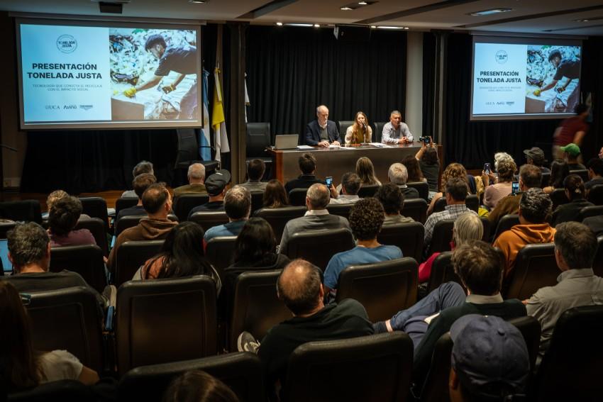 Auditorio lleno en la UCA durante la presentación del proyecto "Tonelada Justa", con tres personas exponiendo en el escenario y pantallas proyectando el título del evento