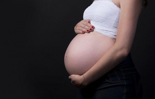Retrato de estudio de una mujer embarazada sosteniendo su vientre sobre un fondo negro.