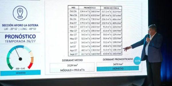 Un hombre presenta una diapositiva con el «Pronóstico Temporada 26/27» para la «Sección Aforo La Gotera». La pantalla muestra una tabla de caudales mensuales (octubre 2026 a septiembre 2027), un medidor de nivel que indica «Húmedo» y comparativas de derrame medio e histórico