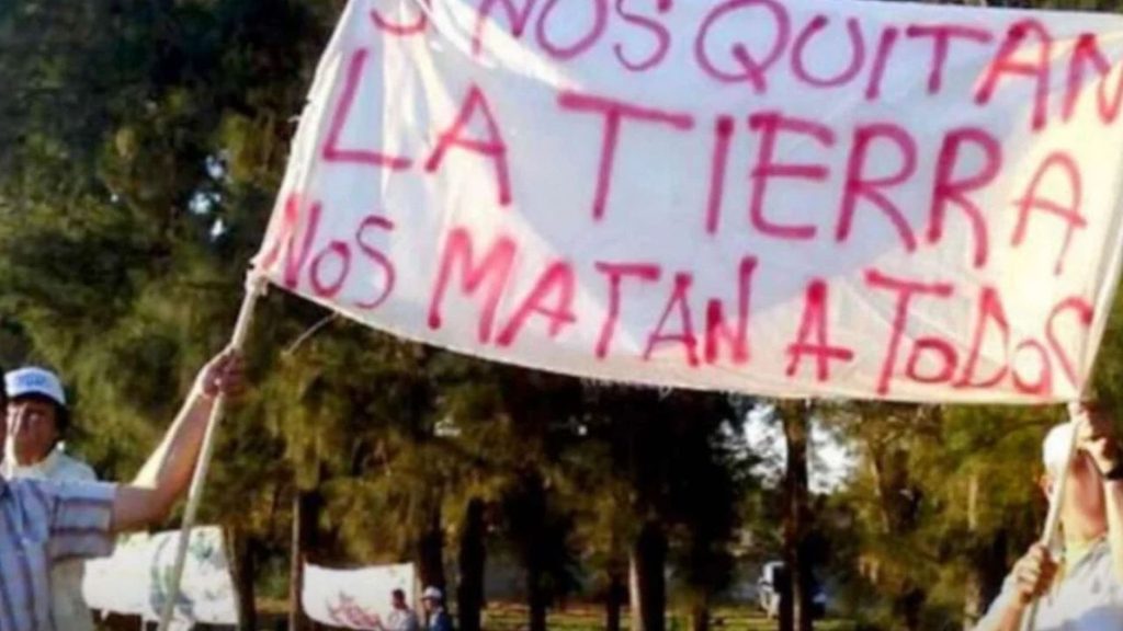 dos personas mantienen en alto una bandera que dice: "si nos quitan las tierras, nos matan a todos"