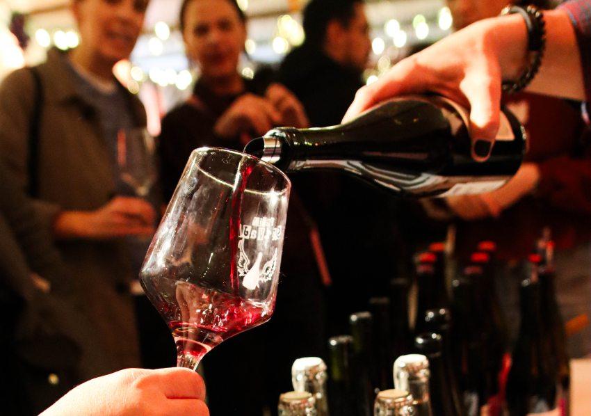 Una mano sirve vino en una copa transparente.