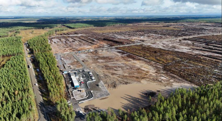Vista aérea de un amplio terreno forestal deforestado y despejado para obras de construcción, adyacente a un bosque frondoso de pinos.