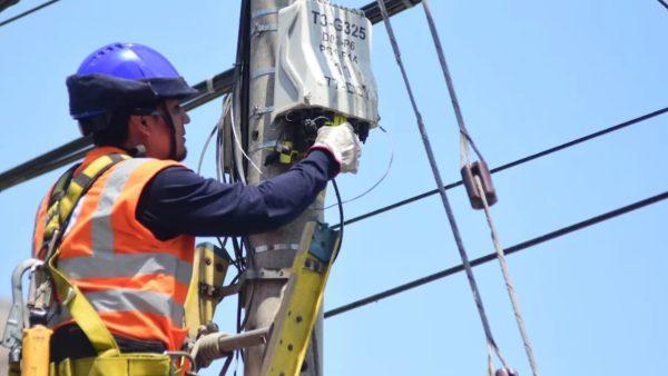 Técnico con casco, guantes y chaleco reflectante realiza tareas de mantenimiento en un poste de infraestructura eléctrica