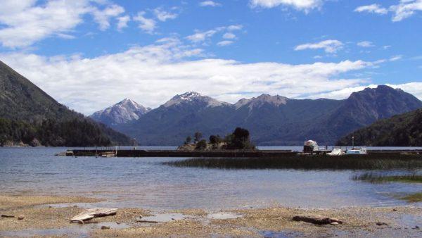 Vista panorámica del lago Moreno en Bariloche, rodeado de bosques patagónicos y montañas, con una costa de aguas tranquilas