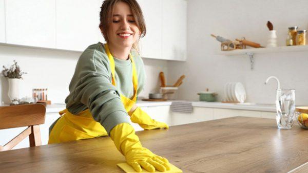 una chica está limpiando la mesada de la cocina con un trapo amarillo