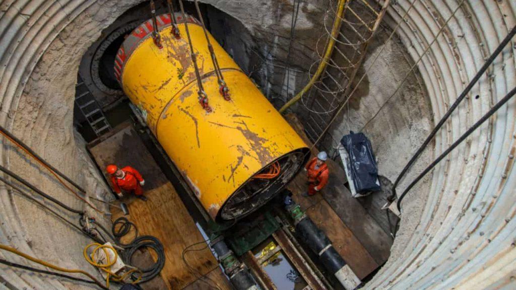 Operarios trabajan en la instalación de una gran estructura cilíndrica amarilla dentro de un pozo de excavación profundo, como parte de una obra hidráulica