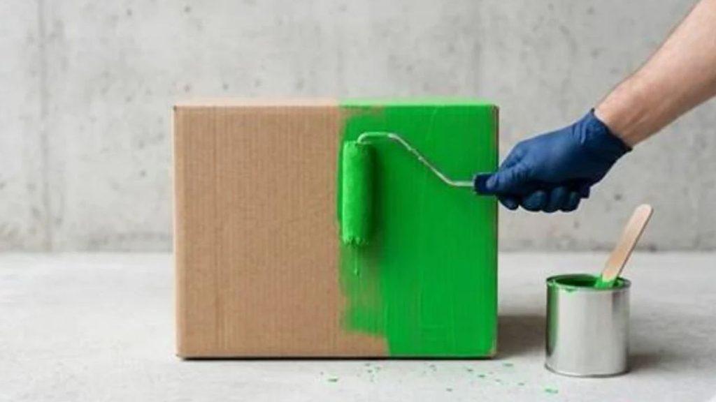 Una mano pinta de verde una caja de cartón, una imagen conceptual que representa el greenwashing