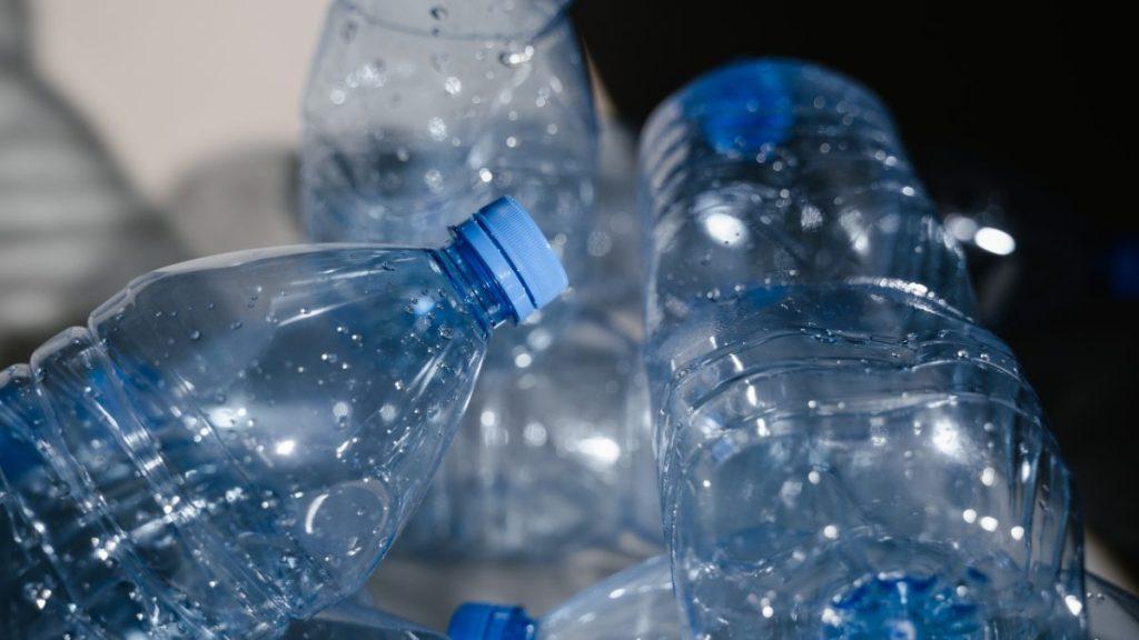 Fotografía de primer plano de varias botellas de plástico pet transparente con tapas azules, apiladas y listas para su reciclaje.