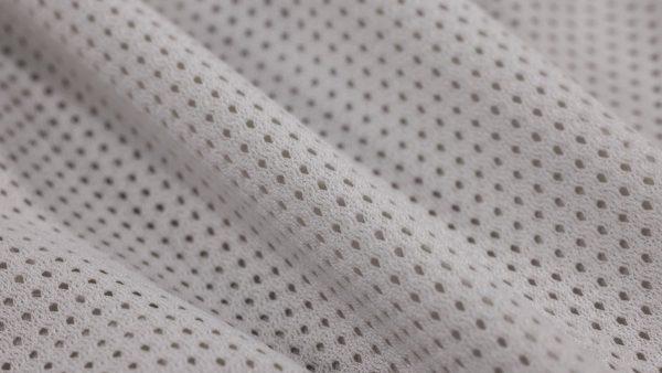 Plano en detalle y de cerca de una tela sintética calada de color beige o gris claro, con pequeños orificios o poros uniformes tipo malla
