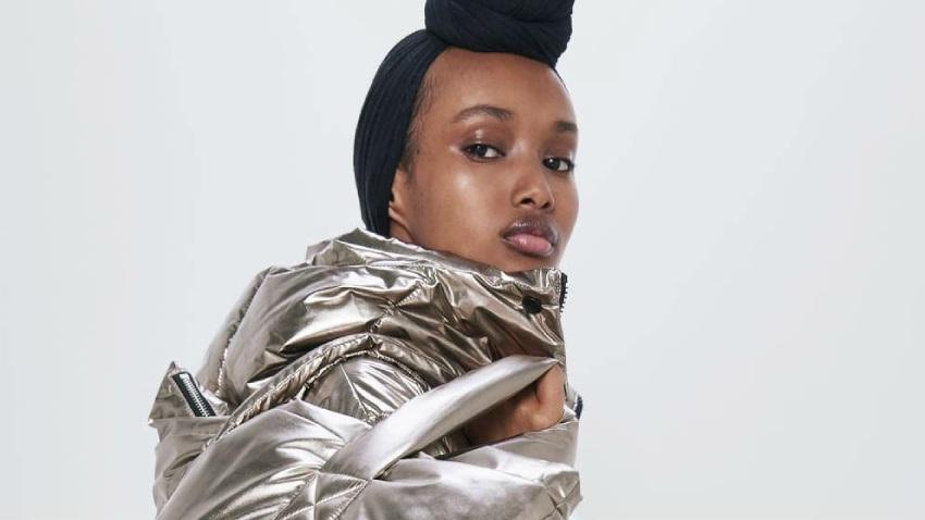 Una modelo viste un abrigo acolchado de tela metalizada en tono dorado brillante y lleva un turbante negro en la cabeza mientras mira hacia la cámara
