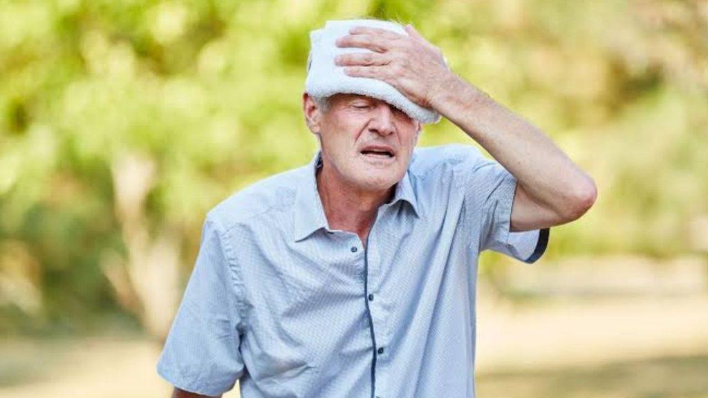 Hombre mayor se seca el sudor de la frente con una toalla en un entorno al aire libre durante un día caluroso