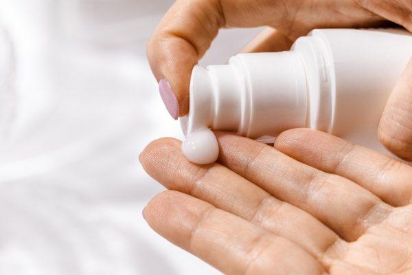 Primer plano de una persona dispensando una gota de crema o protector solar blanco de un envase con dispensador sobre la palma de su mano.